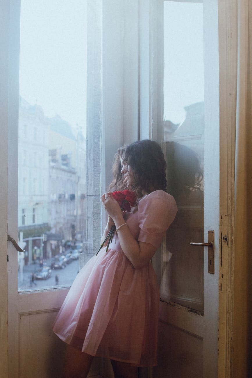 young woman in pink dress by window with flowers